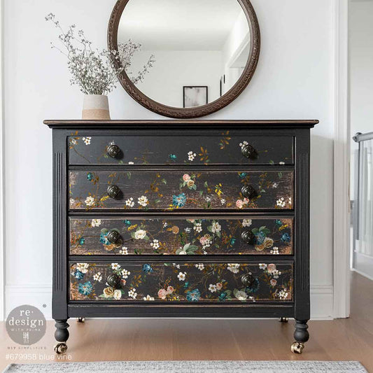 Black dresser with floral patterns and a round mirror above it in a room.