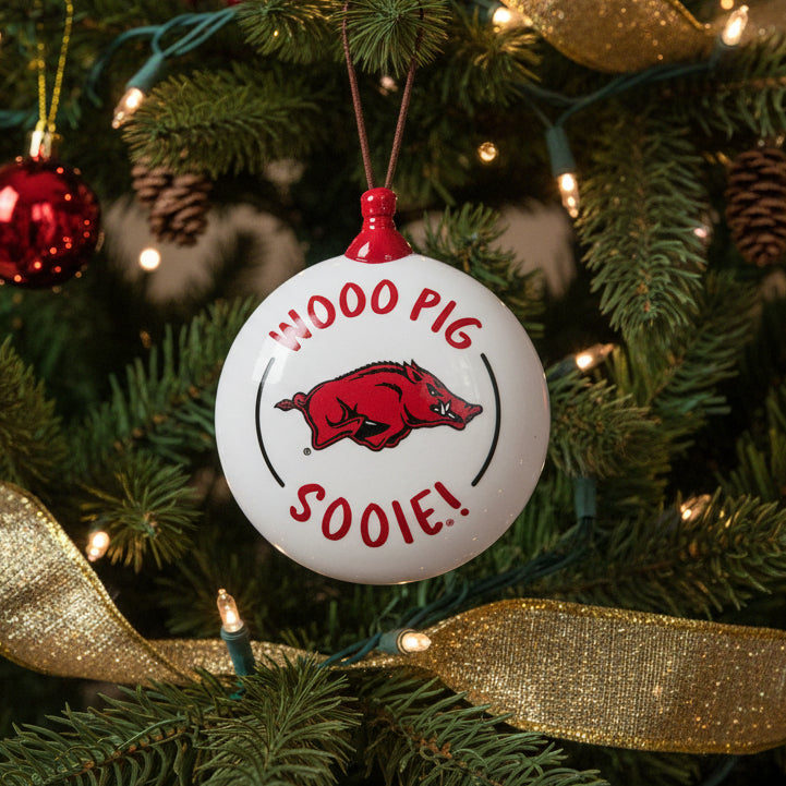 Decorative ornament with 'Wooo Pig Sooie!' text and Arkansas Razorbacks logo on a Christmas tree