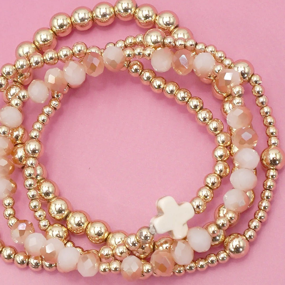 Gold and white beaded bracelets on a pink background