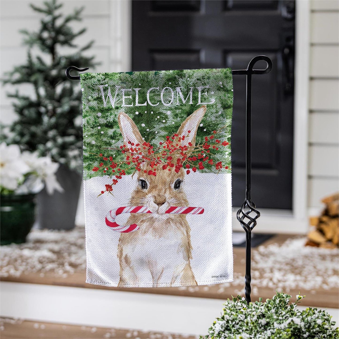 Decorative garden flag with a rabbit holding a candy cane and the word 'Welcome' on a stand outdoors.