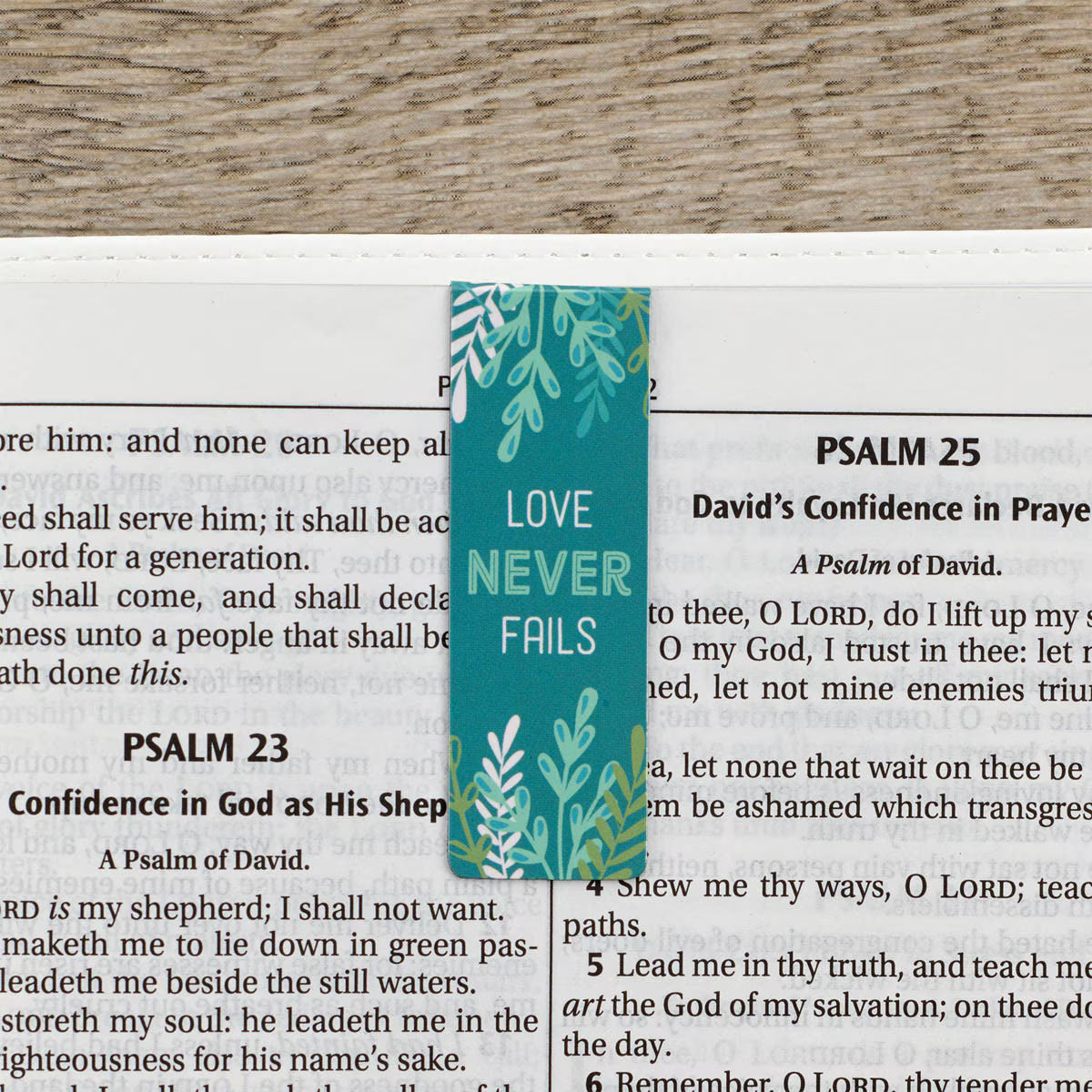 Teal bookmark with 'Love Never Fails' text on a Bible