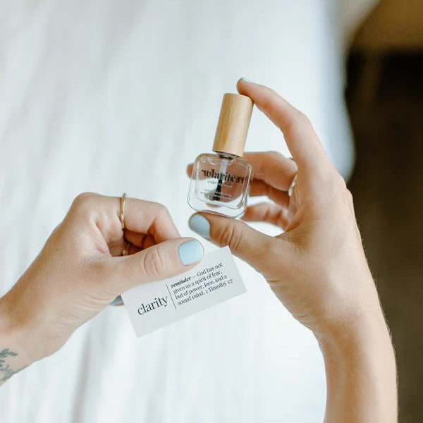 Person holding a bottle of Clarity Top Coat, against a neutral background.