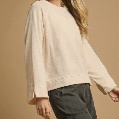 Person wearing a beige sweater and dark pants against a beige background