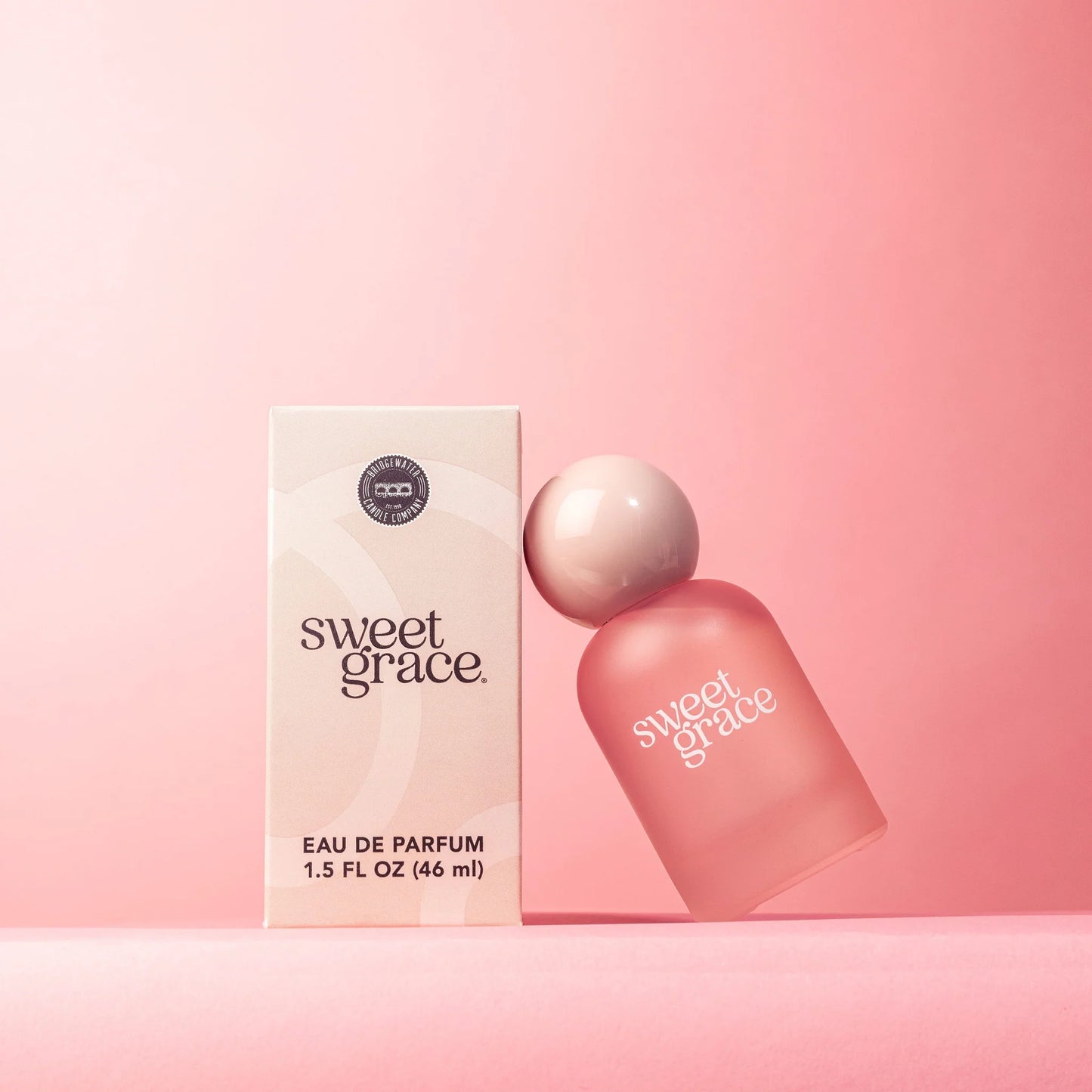 A bottle of Sweet Grace Eau de Parfum with it's box on a pink background