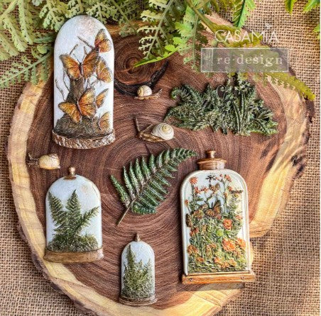 A collection of decorative molds with various natural and artistic designs, displayed on a wooden platter, including floral patterns and insect motifs.