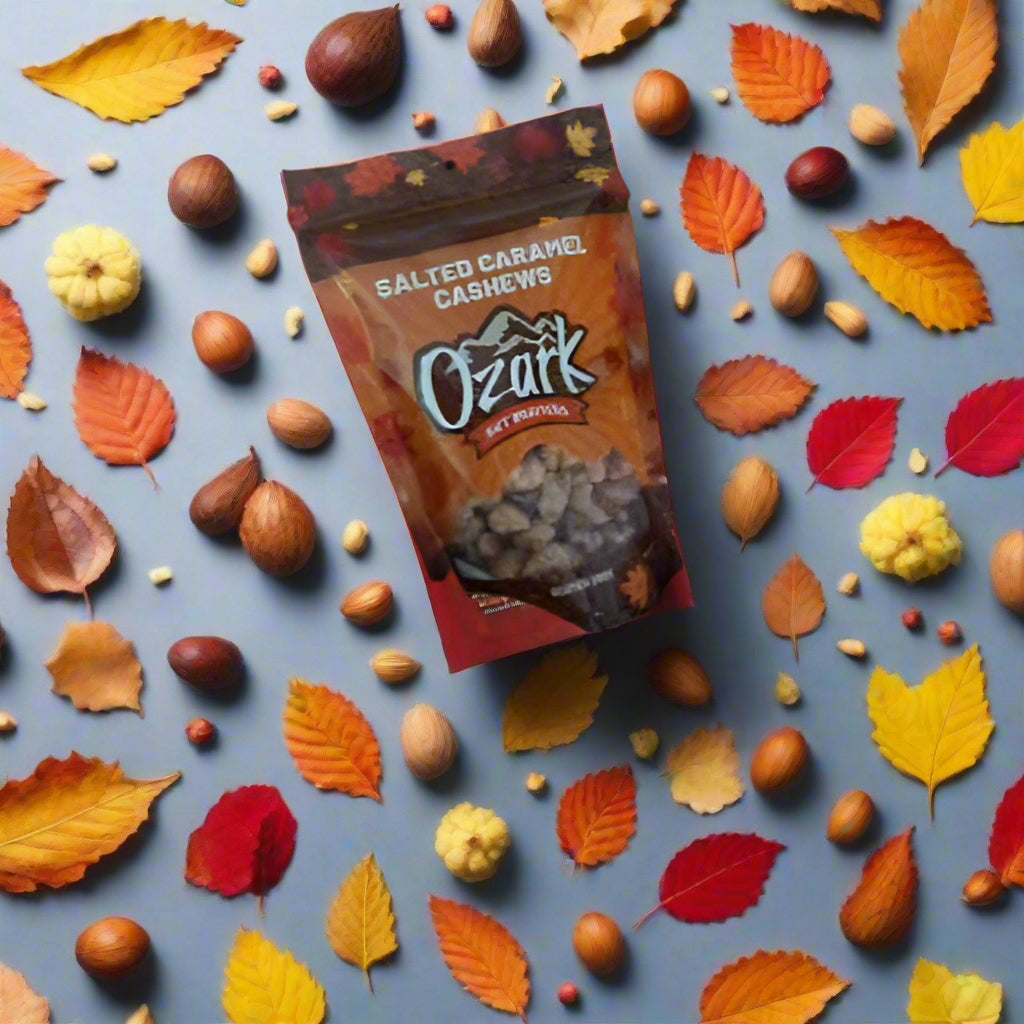 Bag of Ozark Salted Caramel Cashews surrounded by autumn leaves and nuts on a blue background