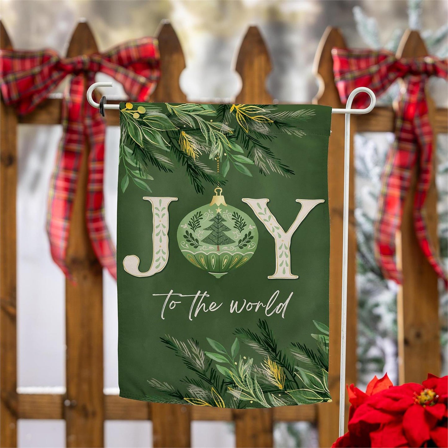 Christmas-themed garden flag with 'Joy to the World' text and festive decorations on a wooden fence.
