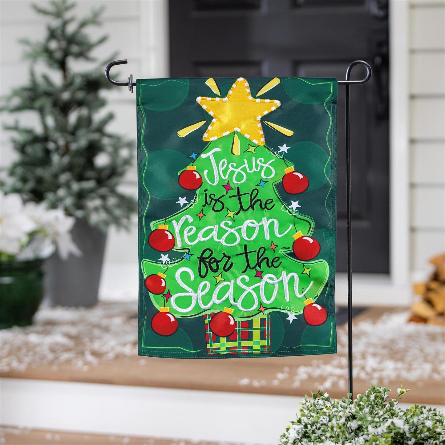 Christmas-themed garden flag with decorative elements and text, placed outdoors.