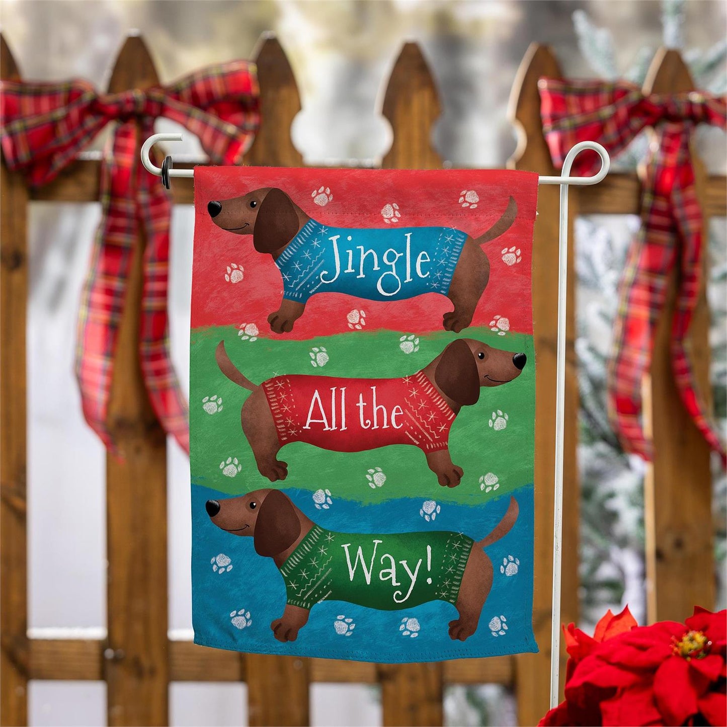 Decorative garden flag with dachshunds in sweaters and text 'Jingle All the Way' on a wooden fence background.