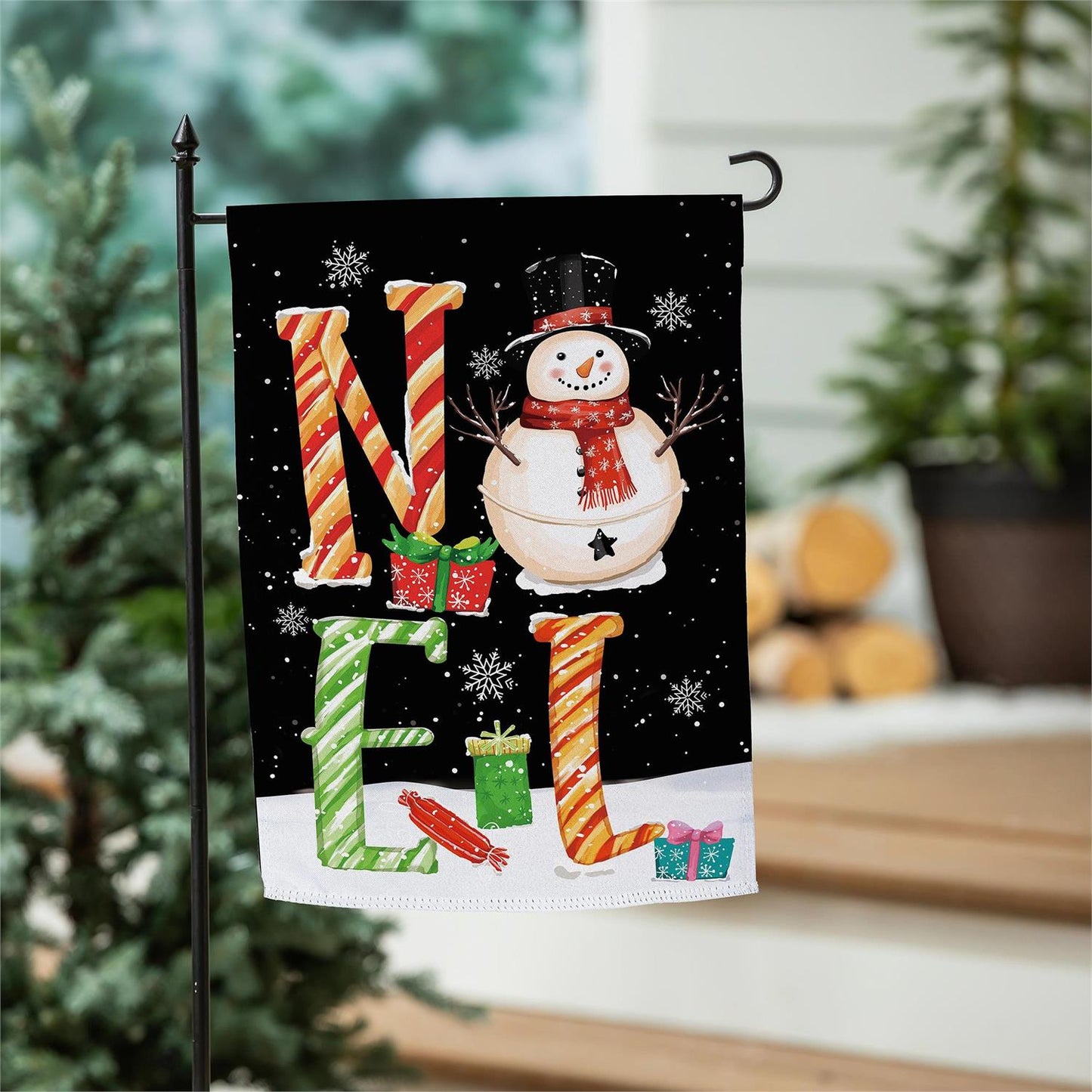 Christmas-themed garden flag with a snowman and candy cane letters in a festive setting.