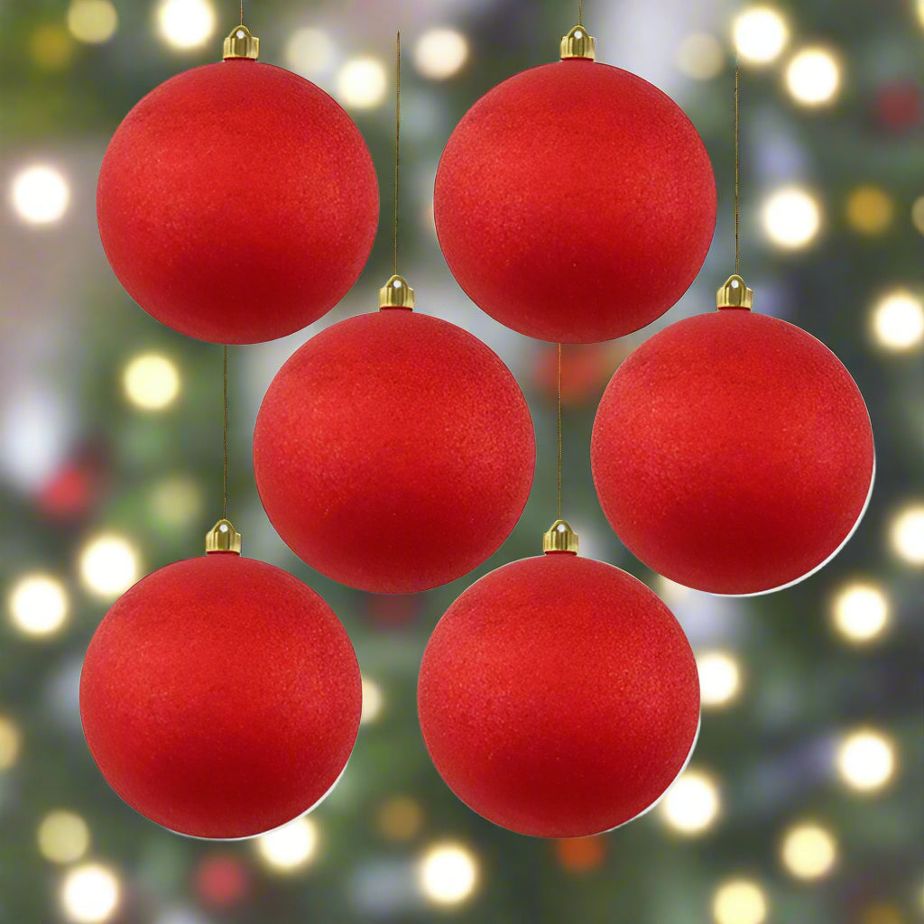 Red Christmas ornaments hanging against a blurred Christmas tree background with lights.