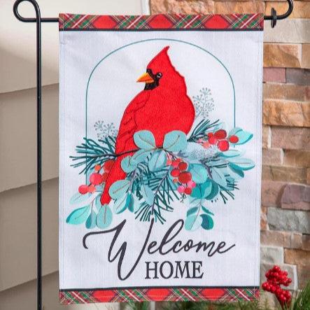 A garden flag with a red cardinal bird sitting on top of a snow-covered branch, with 'Welcome Home' text displayed.