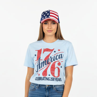 Woman wearing a light blue T-shirt with 'America 1776' design and American flag hat on a white background.