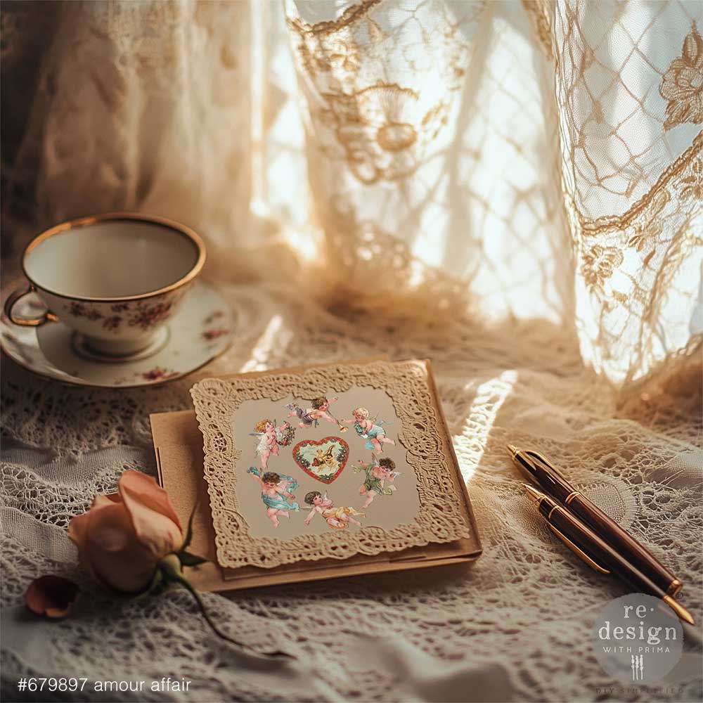 Vintage-style card decorated with Amour Affair transfers on a lace tablecloth with a teacup and pen.