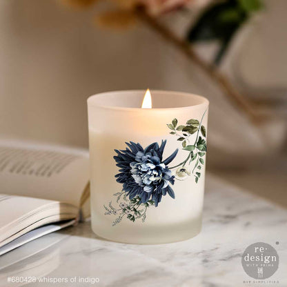 Frosted candle with Whispers of Indigo transfers on a marble surface next to an open book.
