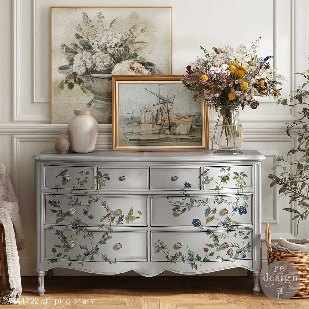 Decorative chest of drawers with Chirping Charm decor transfers, decorated with framed artwork and flowers in a room setting.