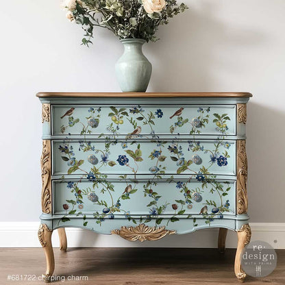 Blue dresser decorated with the Chirping Charm decor transfers on a grey wall with a vase and flowers on top.