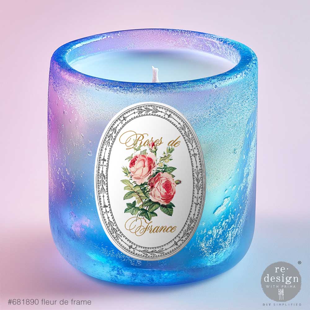 Candle in a blue glass holder with Fleur De Frame Luxe Transfers on a light pink background