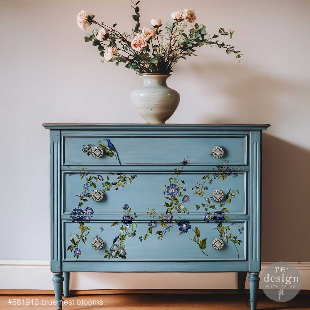 Blue dresser with the Blue Nest Blooms middy transfer with vase of flowers on top against a plain wall.