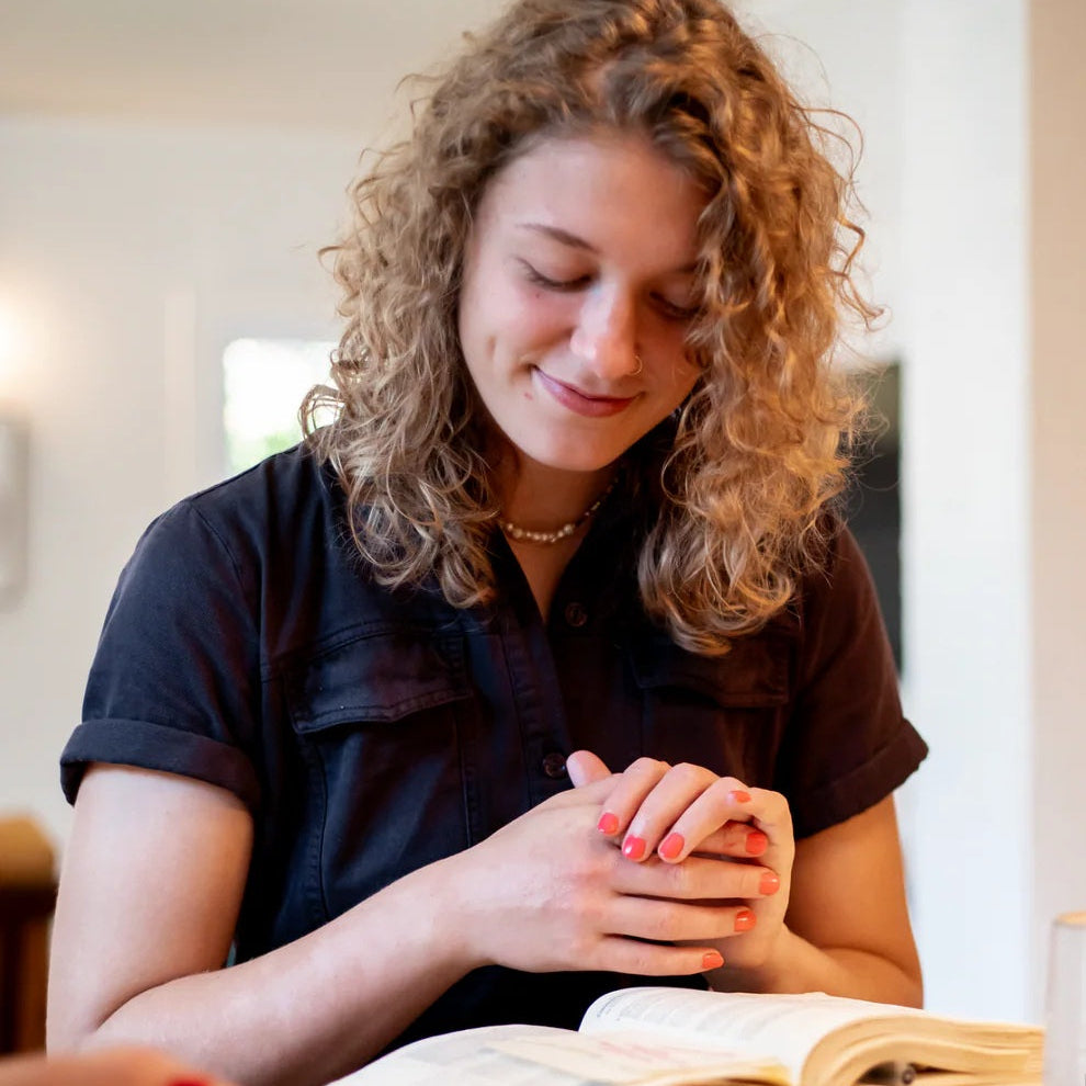 Woman sitting at a table with an open Bible, smiling.