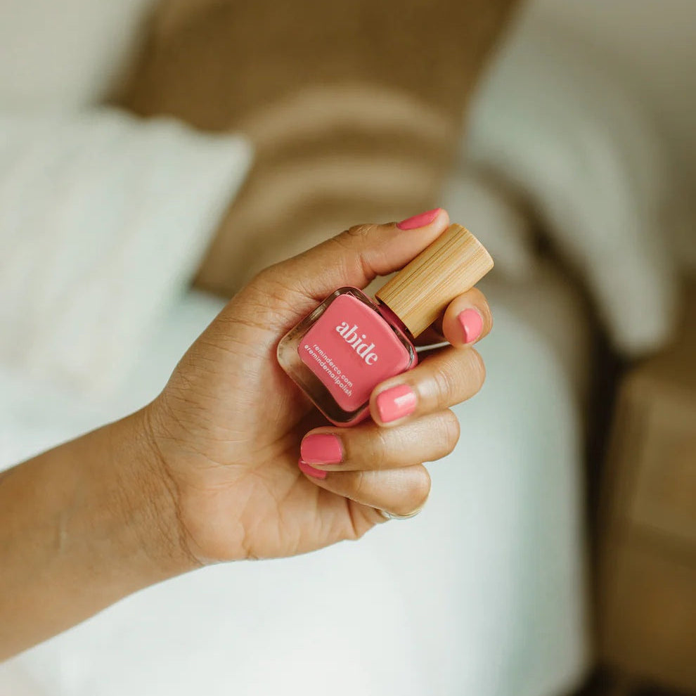 Hand holding a bottle of Reminder Nail Polish in the color Abide with a blurred background.