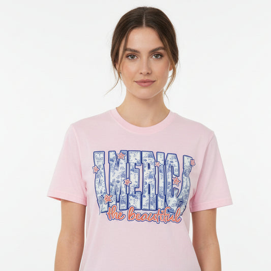 Woman wearing a light pink t-shirt with "America the beautiful" graphic design on a white background.