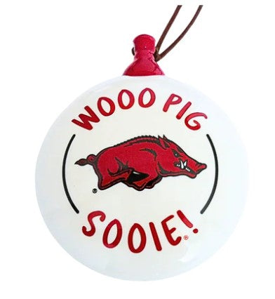 A ceramic holiday ornament with a white background featuring the text 'WOOO PIG SOOIE!' and a red and black illustration of a razorback (a type of pig) alongside the Arkansas logo.