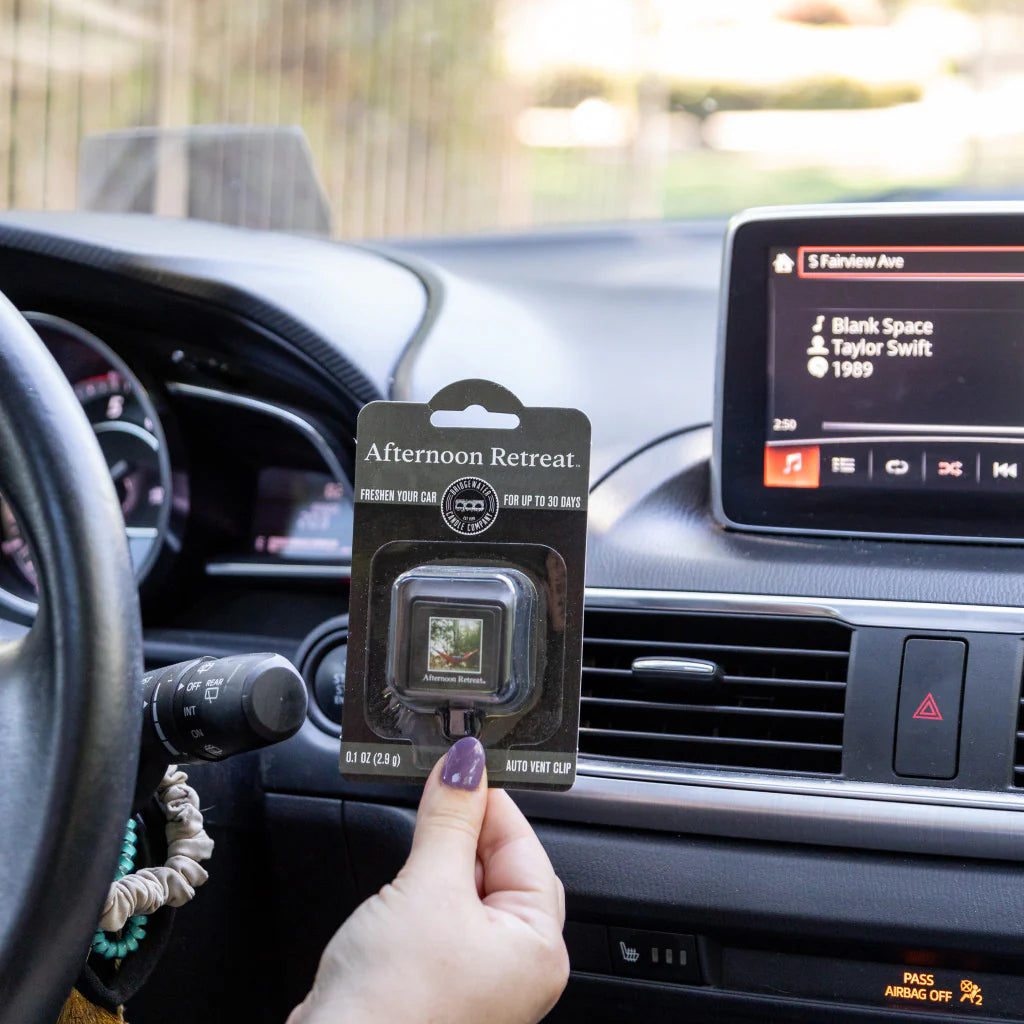 A hand holding an Afternoon Retreat Auto Car Clip up to a car dashboard