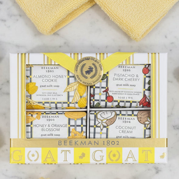 Beekman 1802 Goat Milk Bar Soap set in a gift box on a marble surface. Scents include Almond Honey Cookie, Coconut Cream, Honey & Orange Blossom, and Pistachio & Dark Cherry.