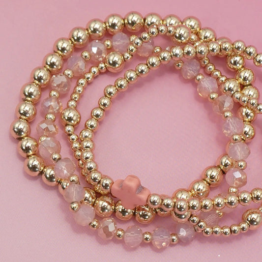 Gold beaded bracelets on a pink background