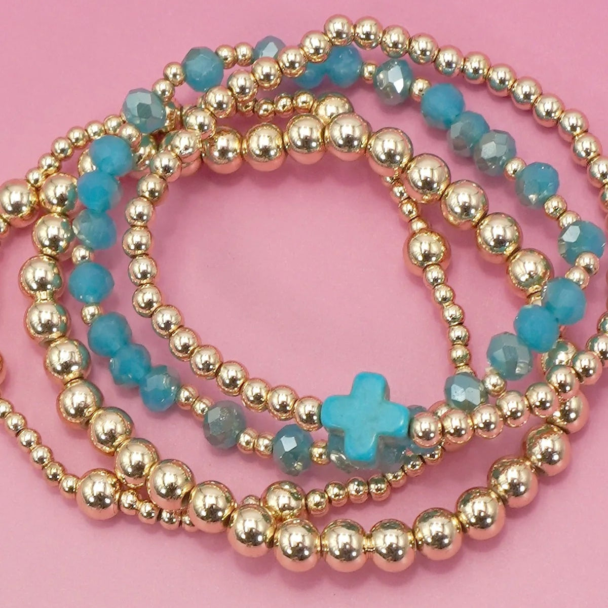 Gold and turquoise beaded bracelets on a pink background