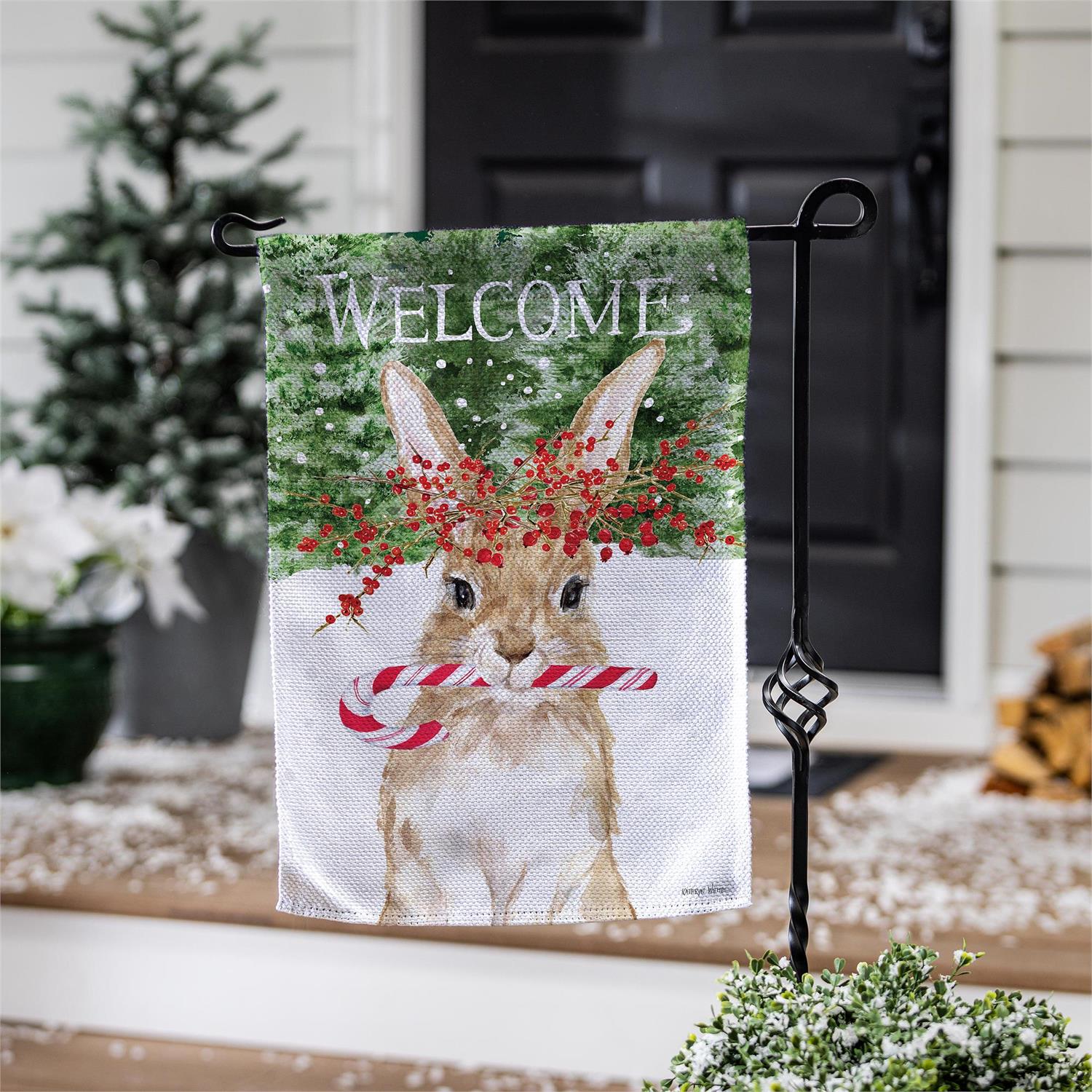 Decorative garden flag with a rabbit holding a candy cane and the word 'Welcome' on a stand outdoors.