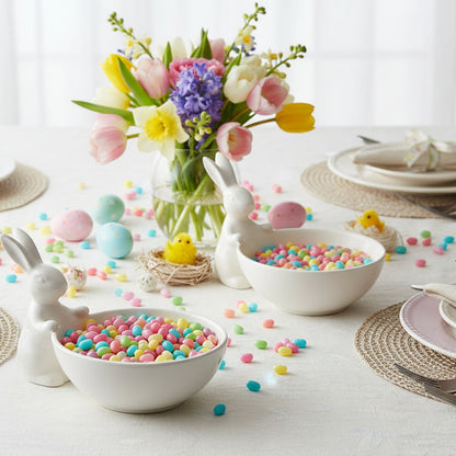 Two white ceramic rabbit bowls filled with jelly beans on a table with flowers