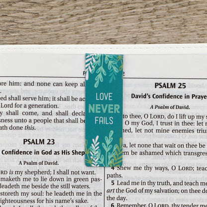 Teal bookmark with 'Love Never Fails' text on a Bible