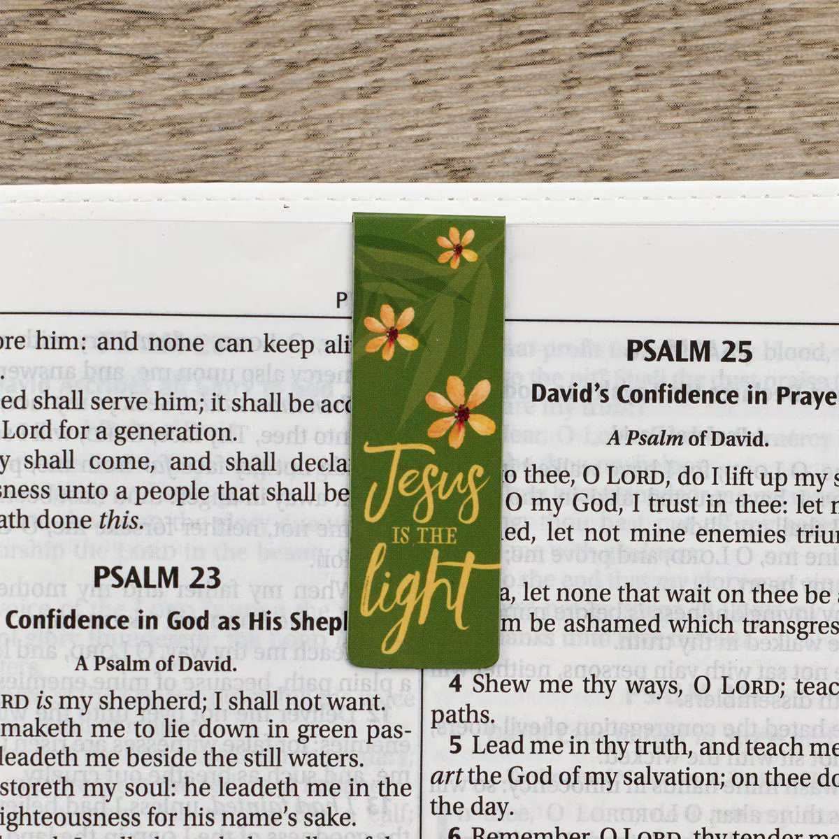 Green bookmark with floral designs and 'Jesus is the light' text on a Bible page.