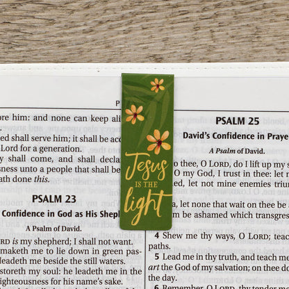 Green bookmark with floral designs and 'Jesus is the light' text on a Bible page.