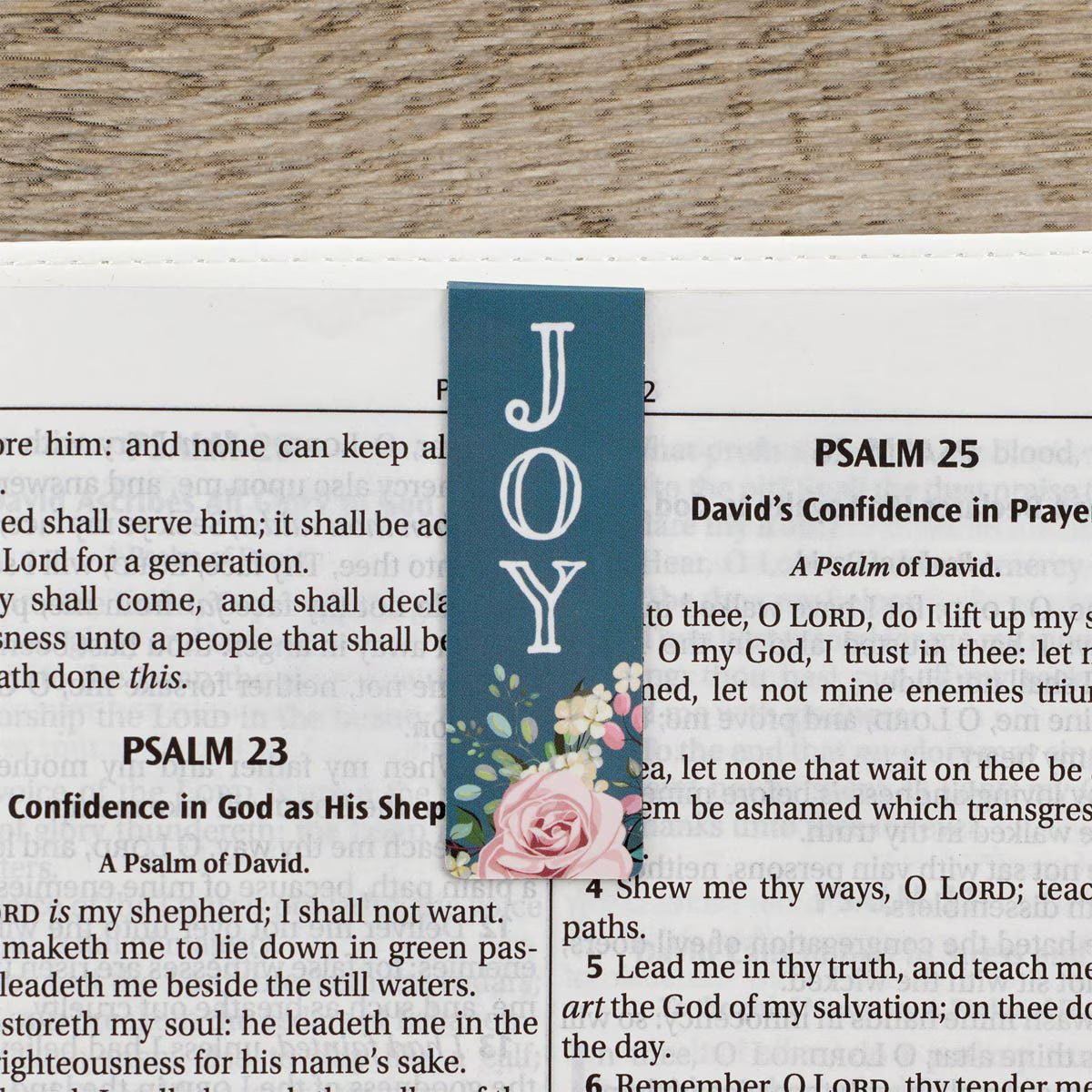 Blue bookmark with floral design and 'JOY' text on a Bible page