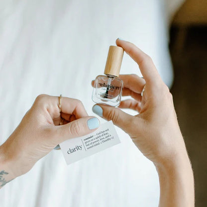 Person holding a bottle of Clarity Top Coat, against a neutral background.