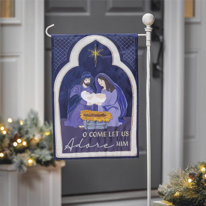 Decorative Christmas flag with nativity scene and 'O Come Let Us Adore Him' text, displayed outdoors.