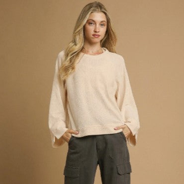 Woman wearing a cream knit crew neck top and dark pants against a brown background
