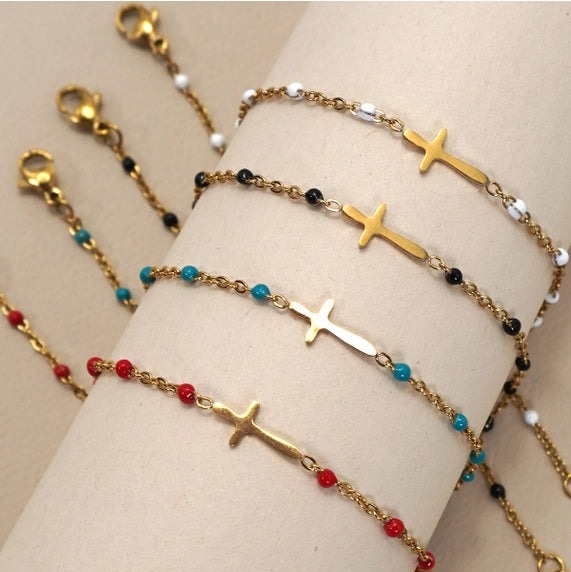 Gold cross bracelets with colored beads on a beige stand