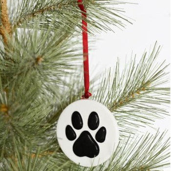White ornament with black paw print hanging on a Christmas tree branch.