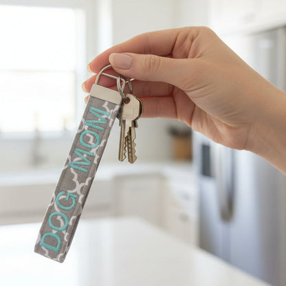 Keychain with 'DOG MOM' text being held in a woman's hand with a kitchen background