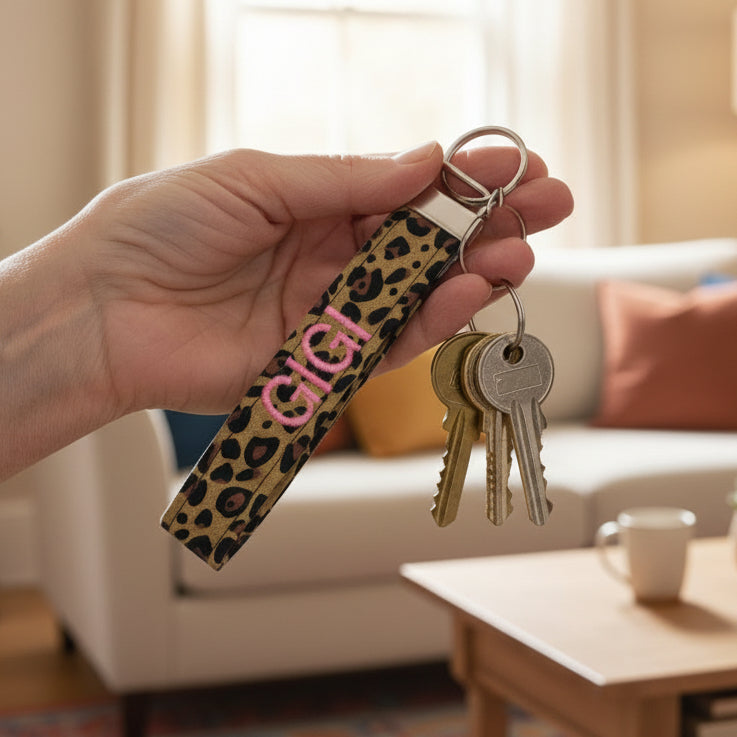Leopard print keychain with 'GIGI' in pink being held by a woman with a living room background