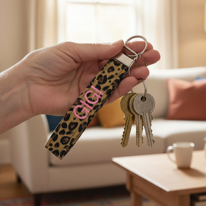 Leopard print keychain with 'GIGI' in pink being held by a woman with a living room background