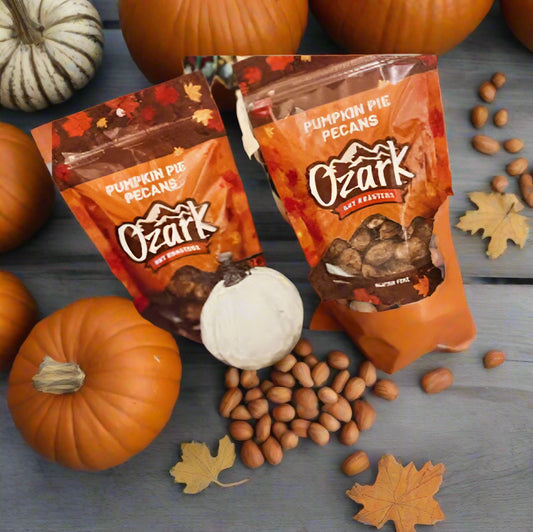 Two packages of Ozark Pumpkin Pie Pecans on a wooden surface with pumpkins and nuts.