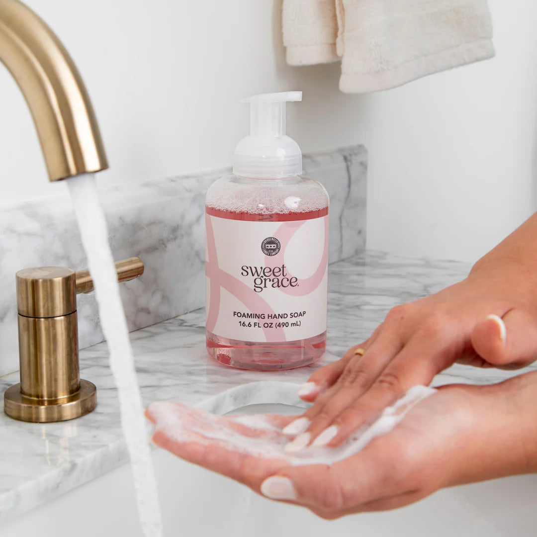 A woman washing her hands with Sweet Grace Foaming Hand Soap in a bathroom sink