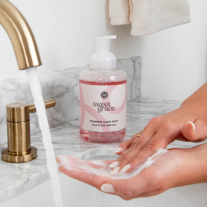 A woman washing her hands with Sweet Grace Foaming Hand Soap in a bathroom sink