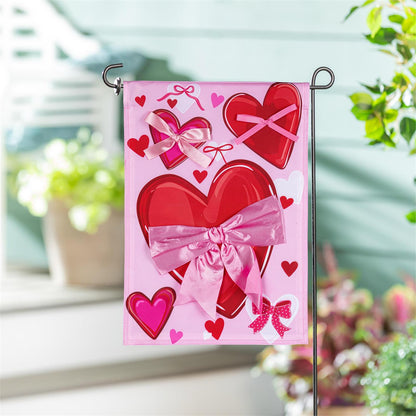 Evergreen Bows & Hearts applique garden flag featuring a design of hearts with bows attached. Flag is shown on a stand.