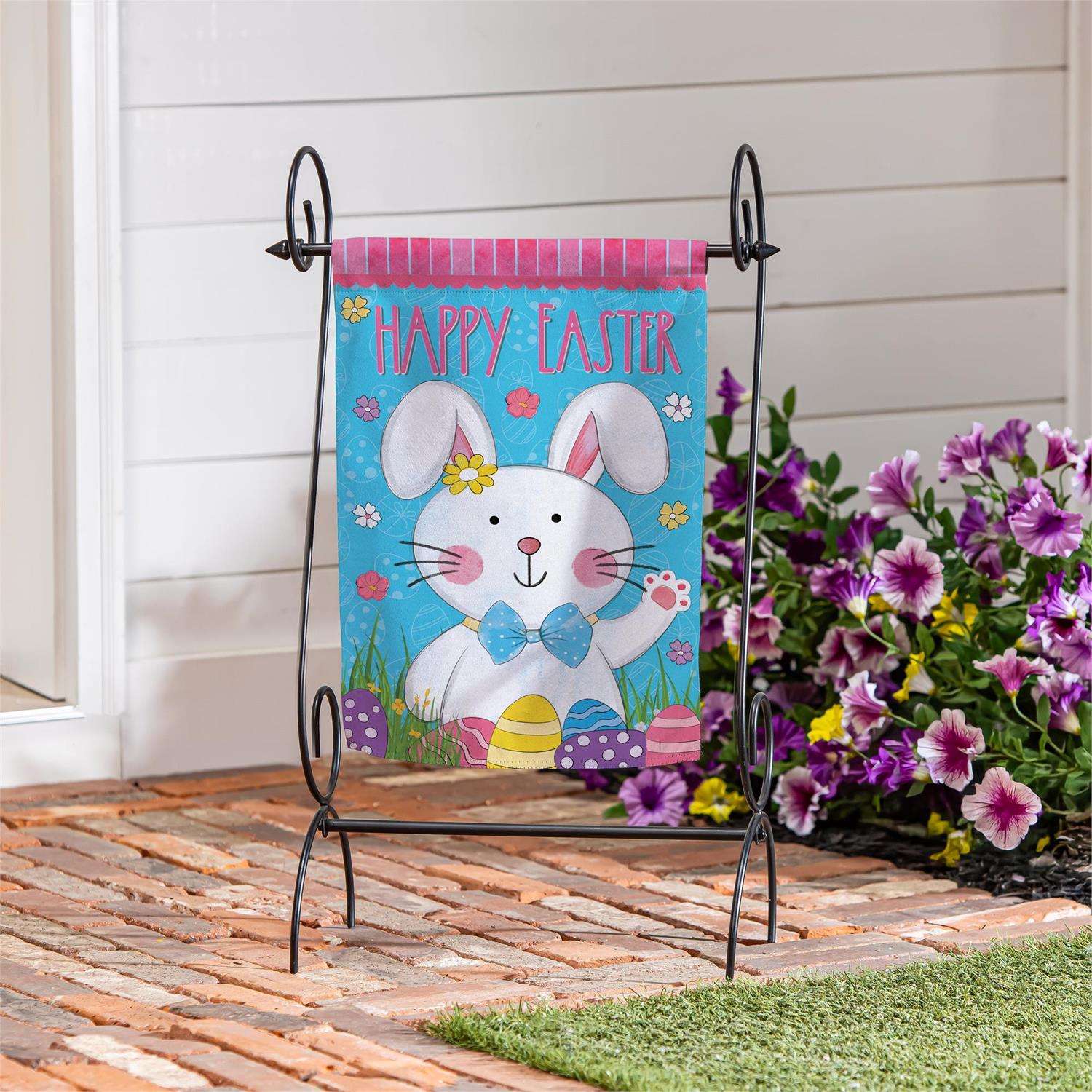 Evergreen Bowtie Bunny garden flag with a bunny on a stand outdoors.